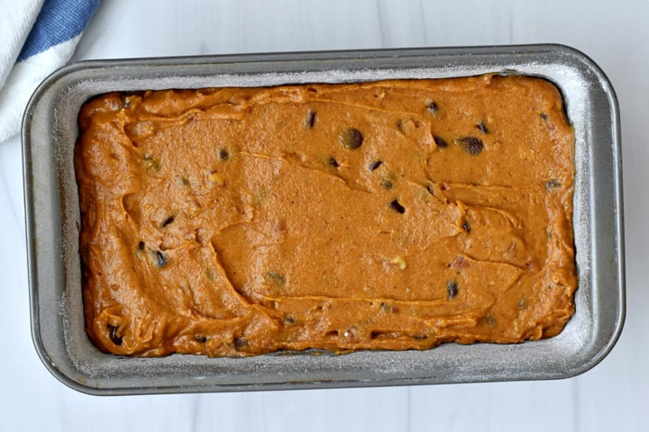 Overhead view of a greased and floured 9x5" loaf pan containing gluten free chocolate chip pumpkin bread batter.