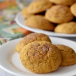 Three gluten free pumpkin snickerdoodles on a small white plate with more cookies in the background.