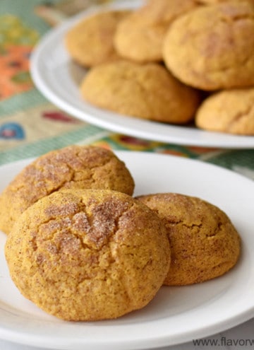 Close up view of three gluten free pumpkin snickerdoodles on a small white plate with more cookies in the background.