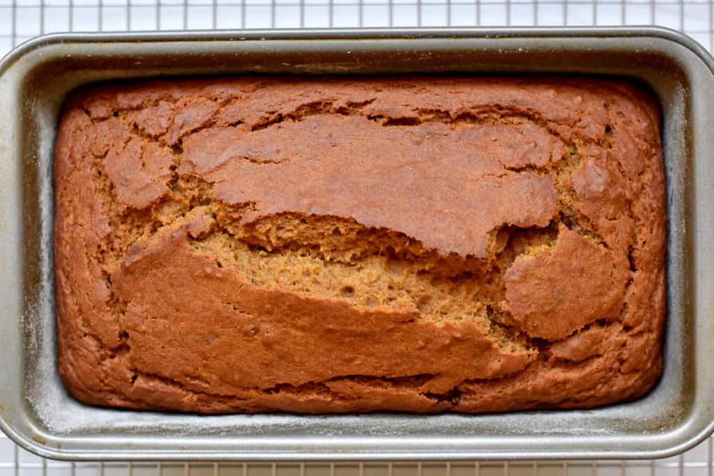 Overhead view of baked loaf of gluten free pumpkin banana bread in loaf pan on cooking rack.
