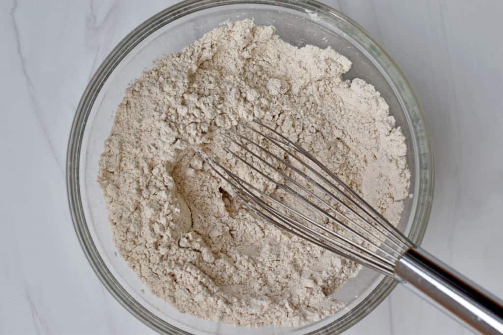 Overhead view of glass mixing bowl containing whisked together gluten free flour blend, pumpkin pie spice, cinnamon, baking soda, baking powder, and salt.,
