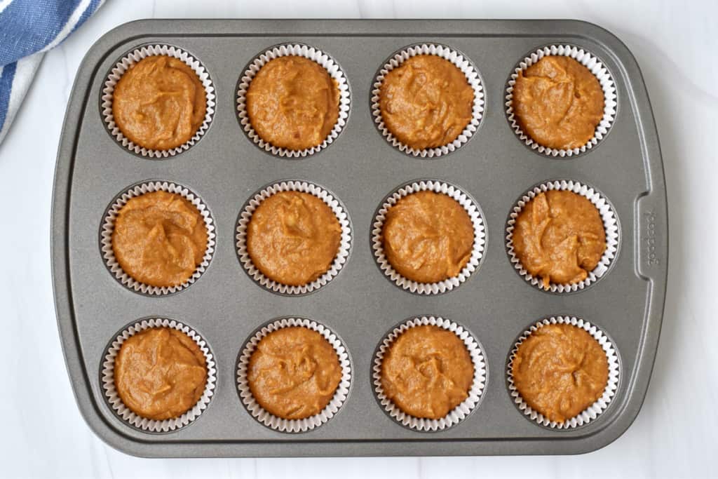 Overhead view of lined muffin pan filled with batter for making gluten free pumpkin banana muffins.