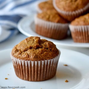 Close up of one gluten free pumpkin banana muffin on small white plate with more muffins in the background.