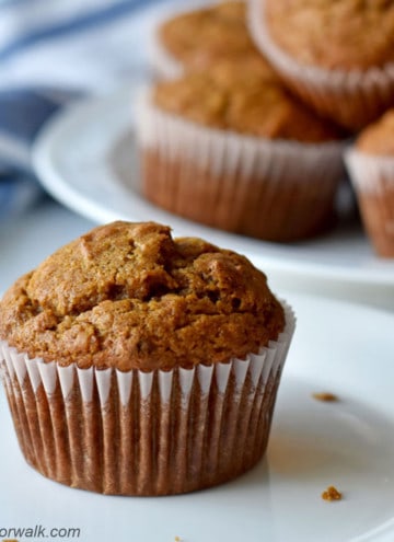 Close up of one gluten free pumpkin banana muffin on small white plate with more muffins in the background.