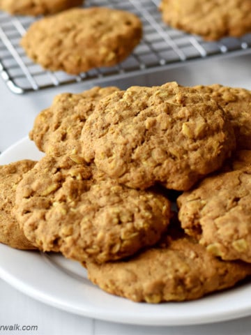 Plate of gluten free pumpkin oatmeal cookies with more cookies on a wire rack in the background.