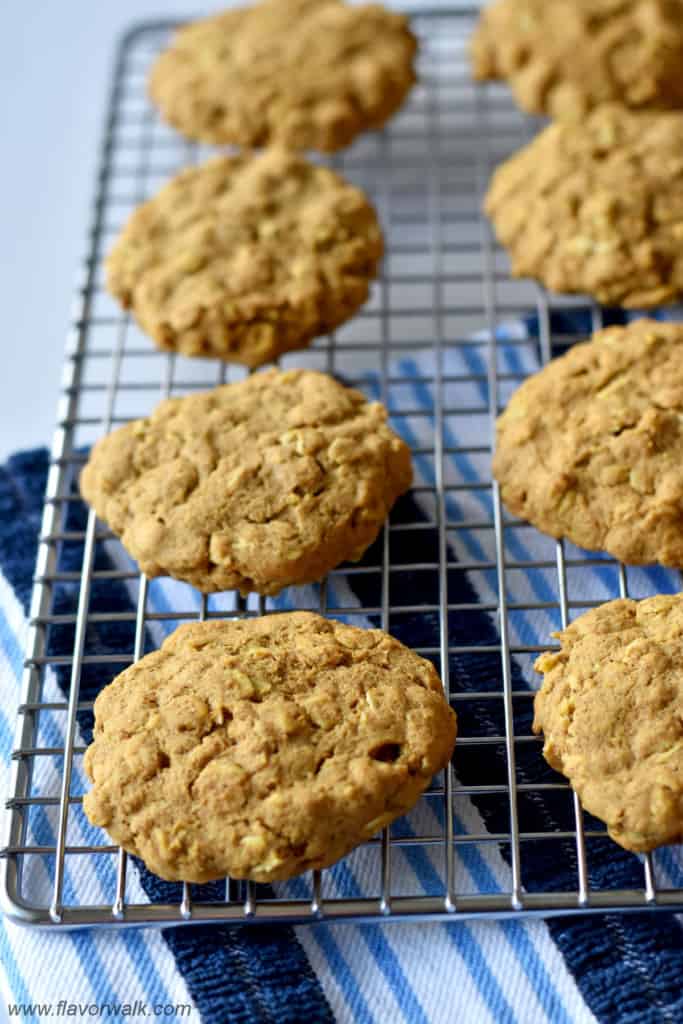 Gluten free pumpkin oatmeal cookies cooling on a wire rack with a blue and white striped kitchen towel under the rack.