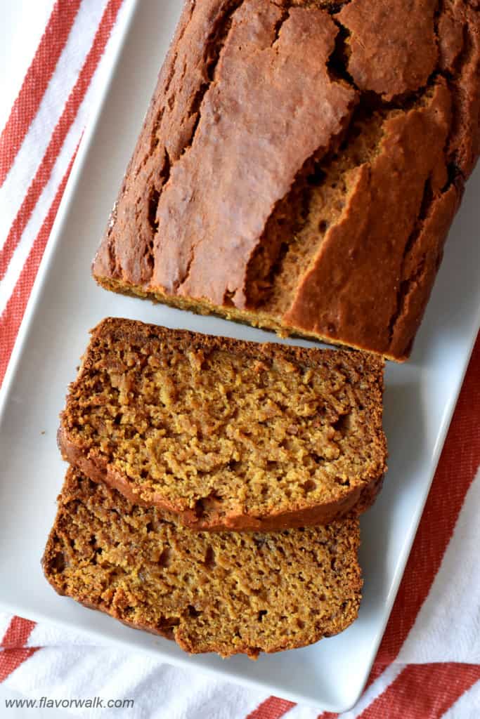 Overhead view of a loaf of gluten free pumpkin banana bread and 2 slices of bread on white rectangular serving platter.