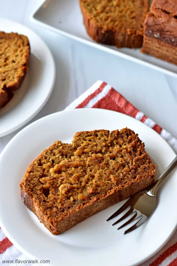 A slice of gluten free pumpkin banana bread and fork on small white plate with more bread in the background.