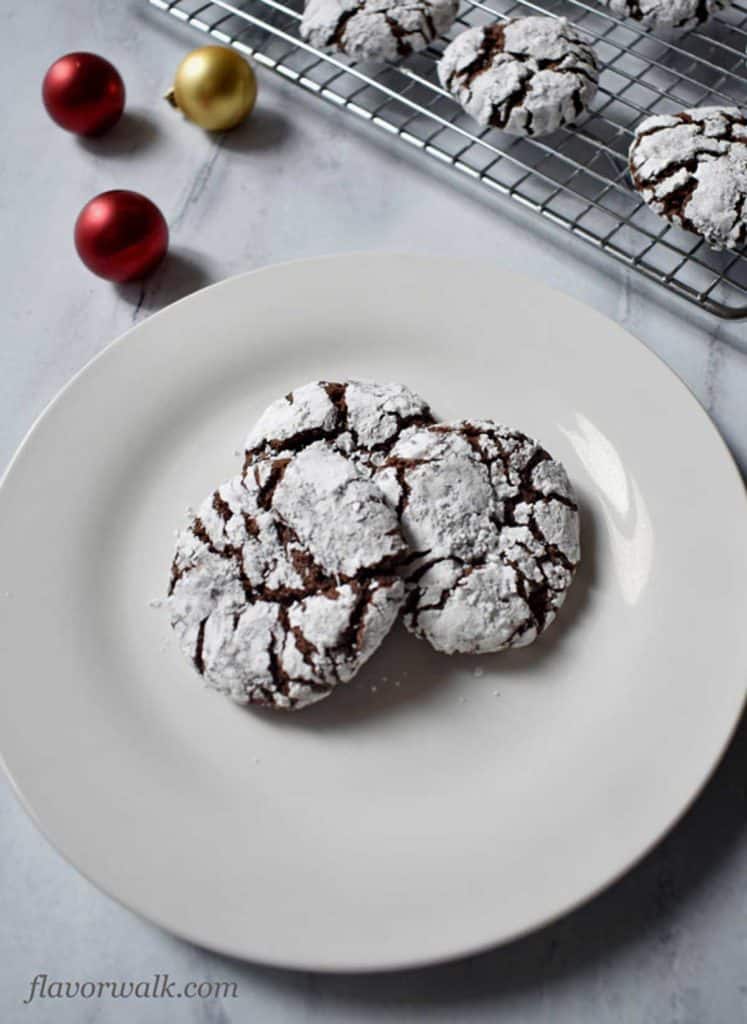 Close up of three gluten free chocolate crinkle cookies on round white plate with more cookies in the background.