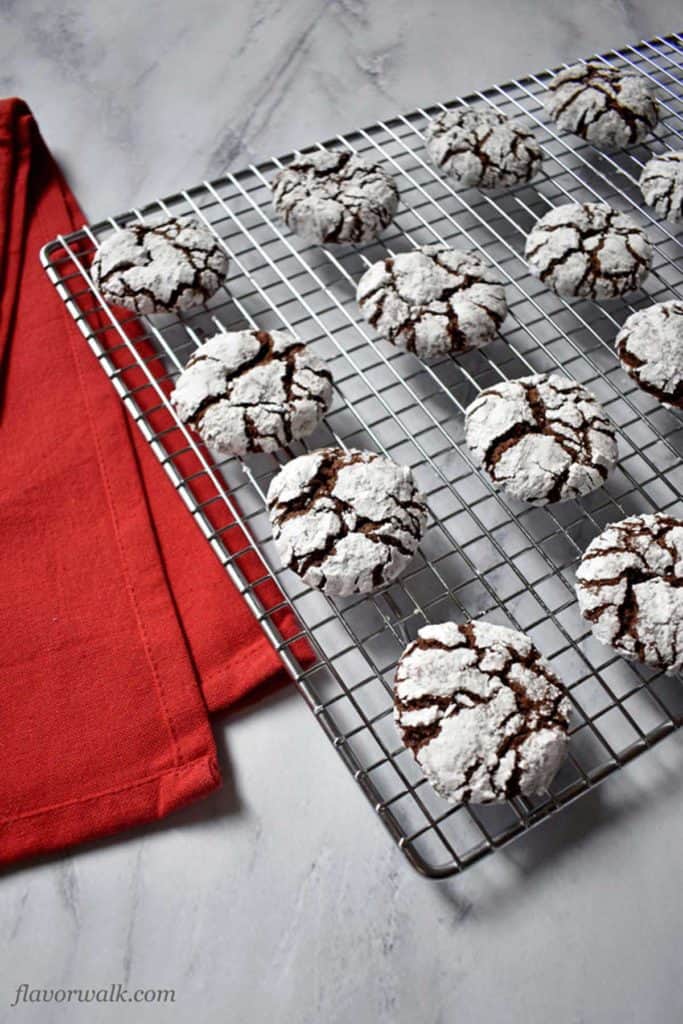 A wire cooling rack filled with gluten free chocolate crinkles with a red kitchen towel on the left.