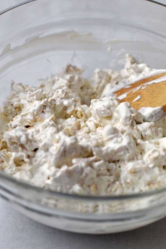 Glass mixing bowl containing mixture of sour cream and rolled oats stirred together.