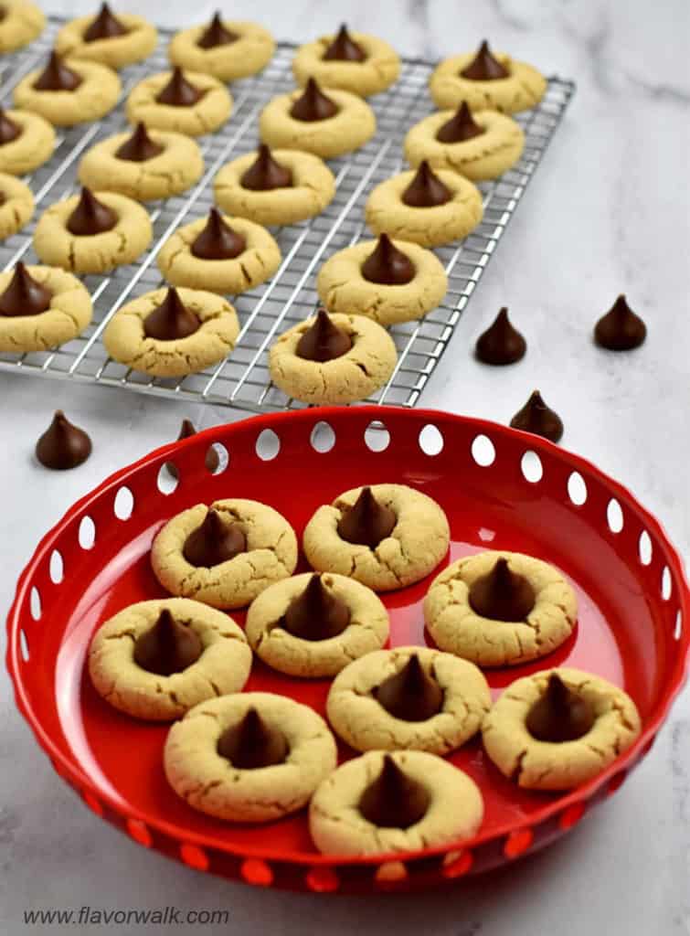 A round red dish filled with gluten free peanut butter blossoms with more cookies and Hershey's kisses in the background.
