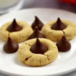 Close up view of gluten free peanut butter kiss cookies and Hershey's kisses on round white dessert plate.