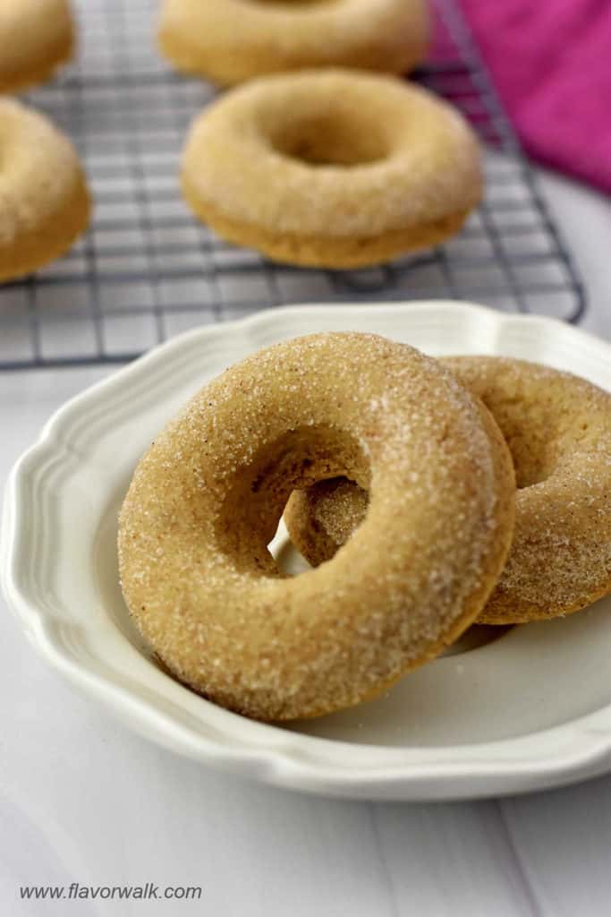 Close-up of two gluten free cinnamon sugar donuts on small white plate with more donuts in the background.