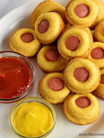 White serving platter containing gluten free mini corn dog muffins and small pinch bowls with ketchup and mustard.