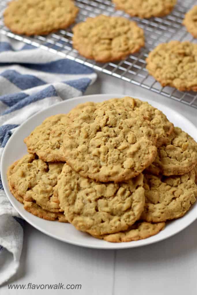 Round white plate with a stack of gluten free peanut butter oatmeal cookies and more cookies on a wire rack in the background.