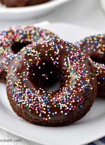 Close-up view of three chocolate donuts with sprinkles on white plate.