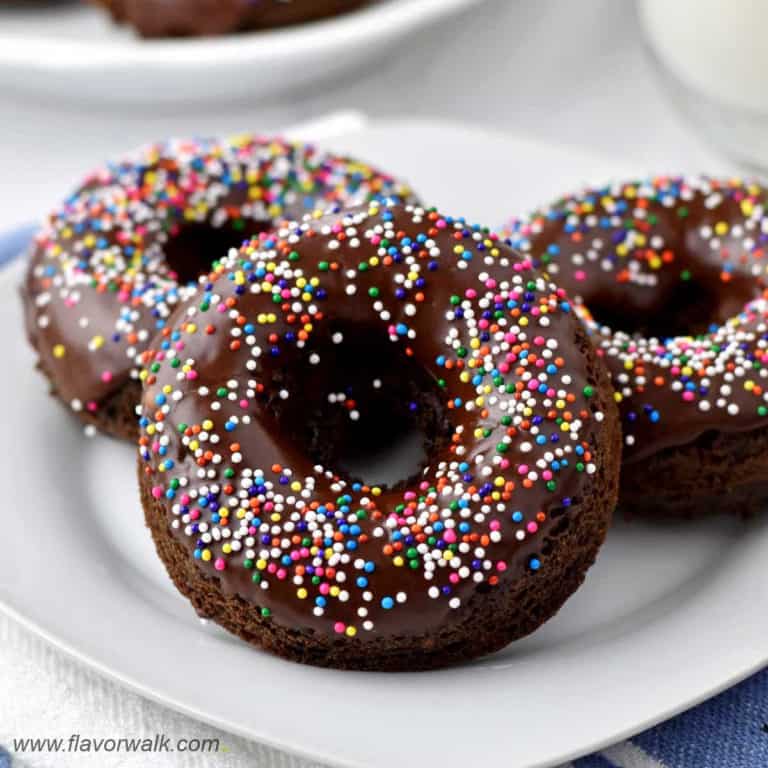 Close-up view of three chocolate donuts with sprinkles on white plate.
