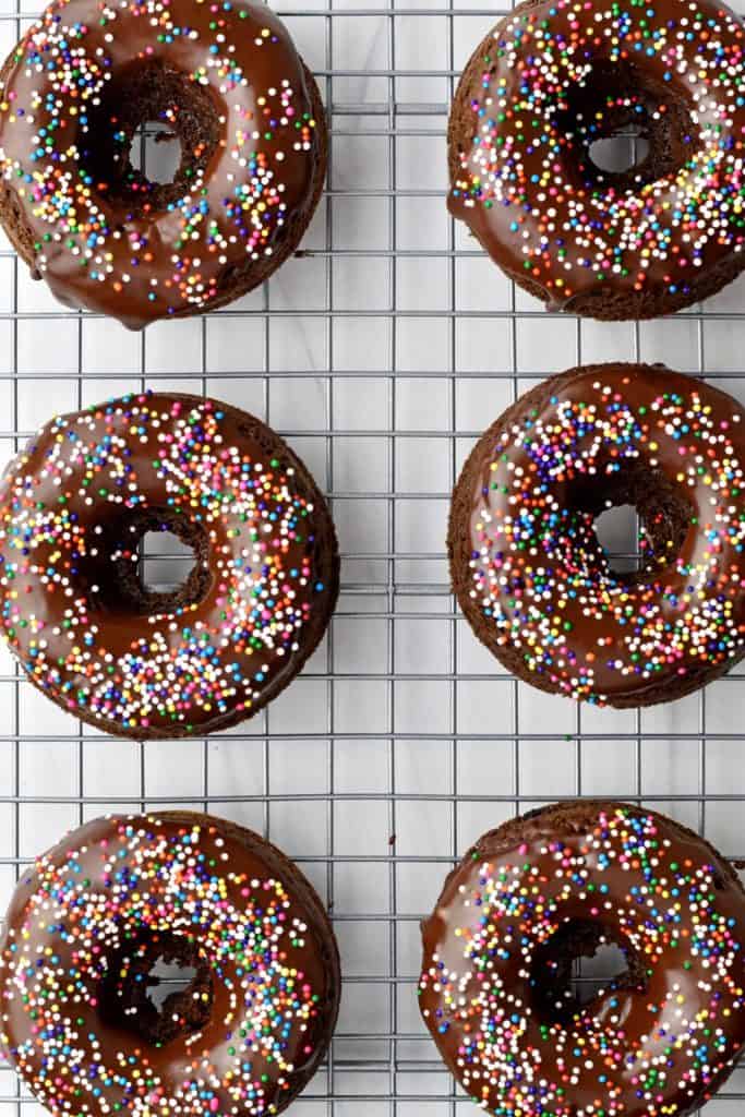 Overhead view of 6 chocolate donuts with sprinkles on wire rack.