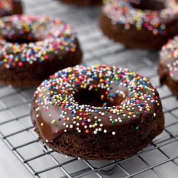 Eye level view of chocolate donuts with sprinkles on wire rack.