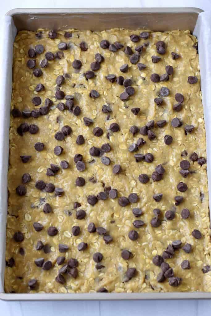 Overhead view of a parchment lined 9x13 baking pan filled with oatmeal chocolate chip cookie dough.