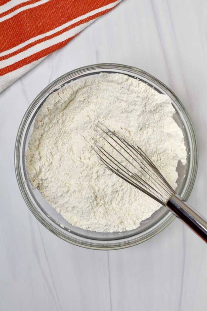 Glass mixing bowl with gluten free flour blend, salt, sugar, and baking powder whisked together.