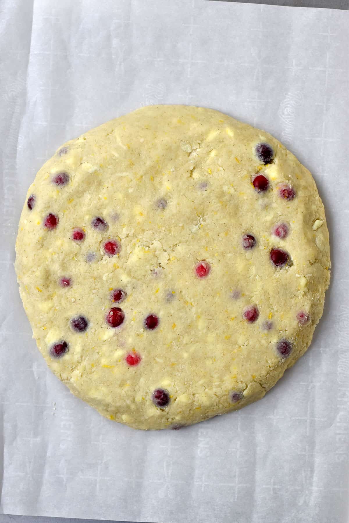 A 10-inch round of cranberry orange scones dough on parchment-lined baking pan.