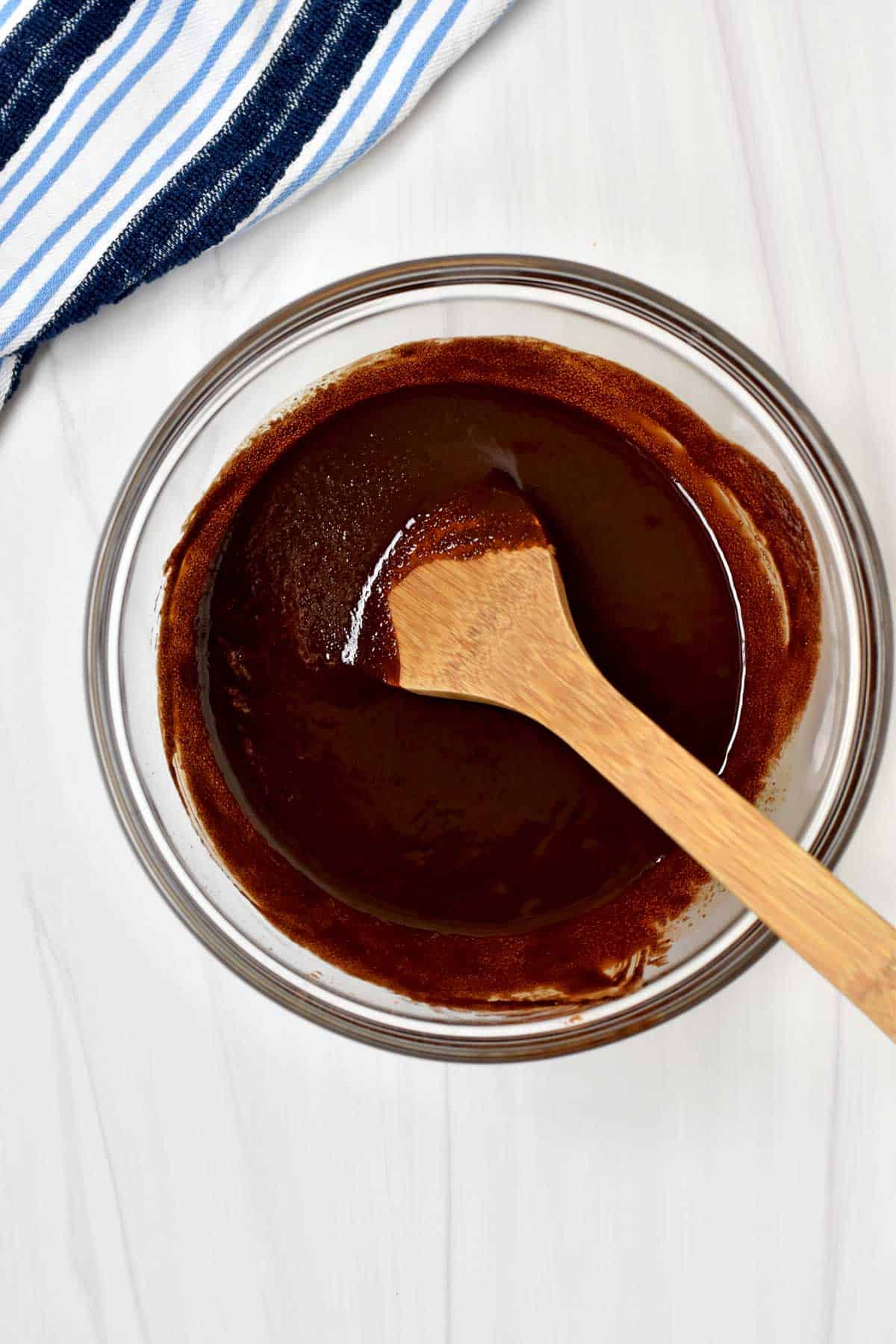 Melted butter, cocoa powder, and sugar stirred together in a glass mixing bowl.