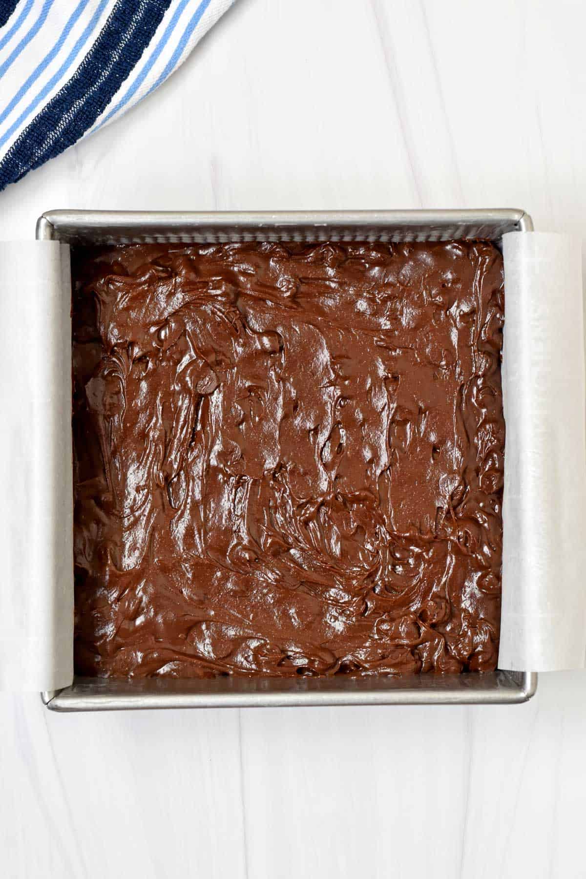 Unbaked gluten free double chocolate brownies batter in parchment lined baking pan.