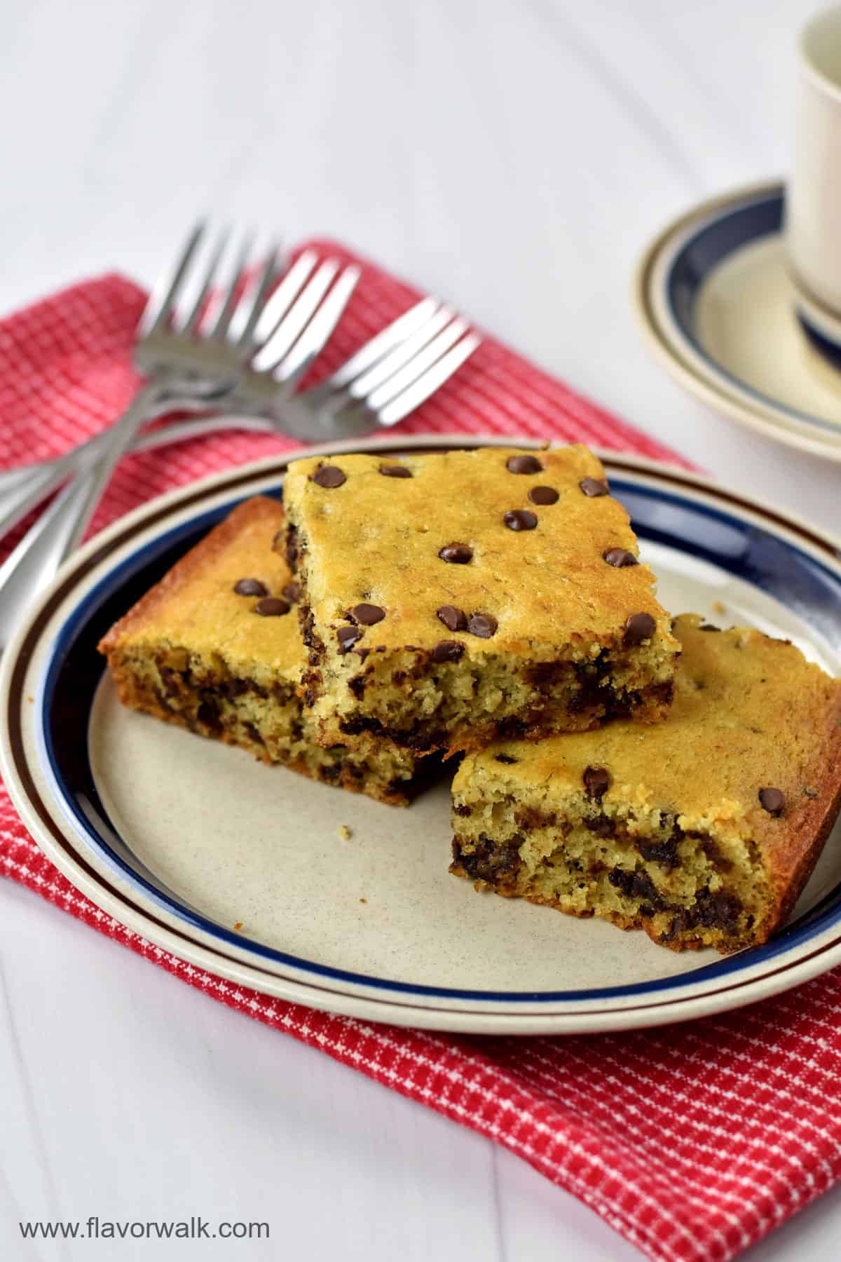 A stack of 3 slices of gluten free snack cake with dessert forks and a coffee cup in the background.