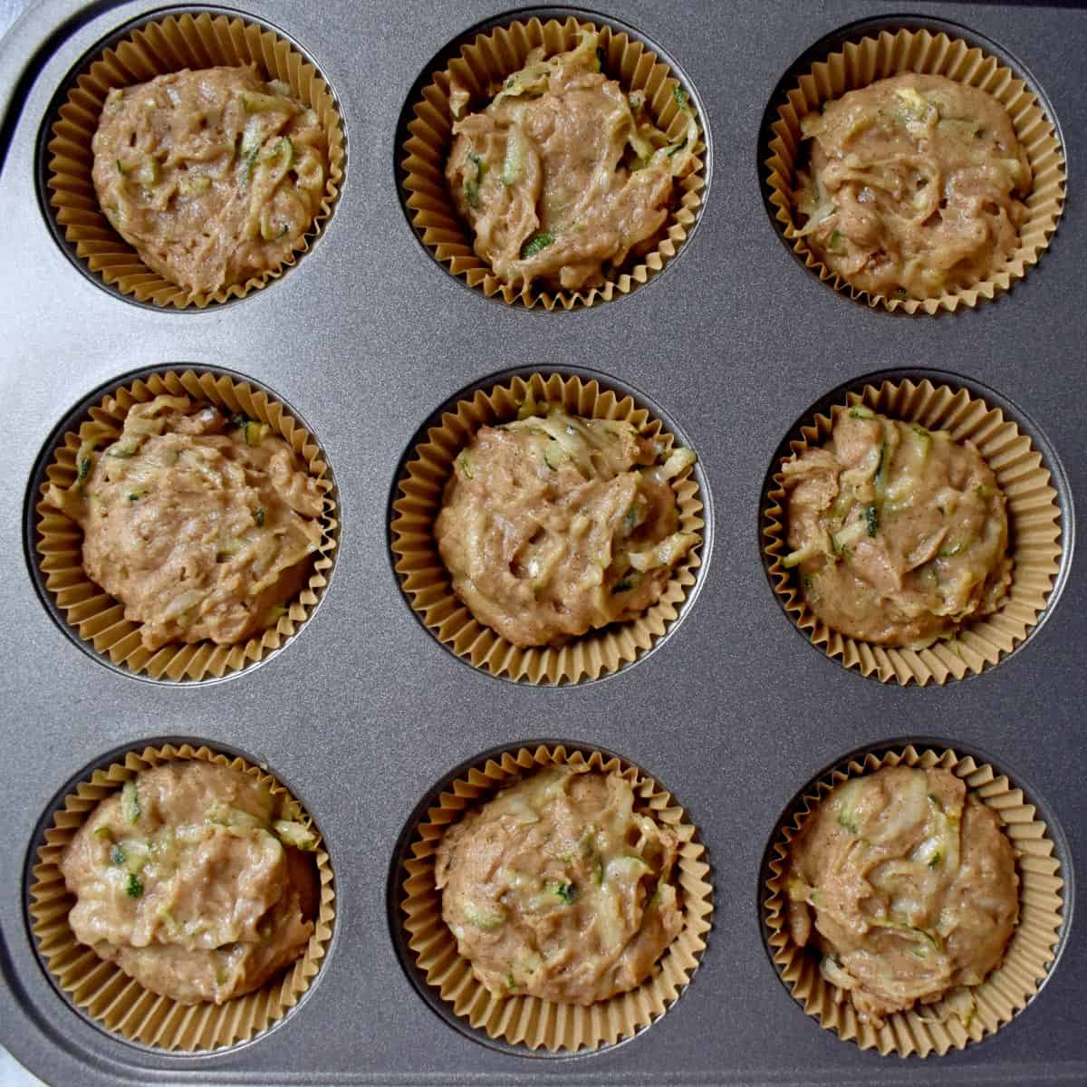 Lined muffin pan filled with gluten free zucchini muffin batter.