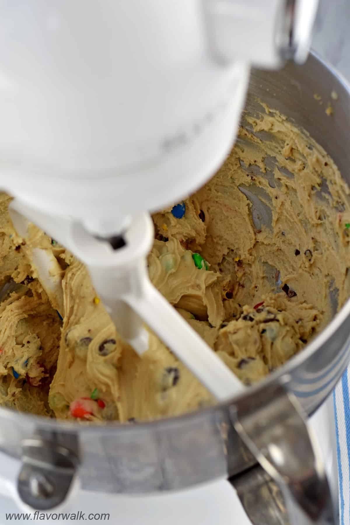 No bake cookie dough with chocolate chips and M&M's in the bowl of a stand mixer.