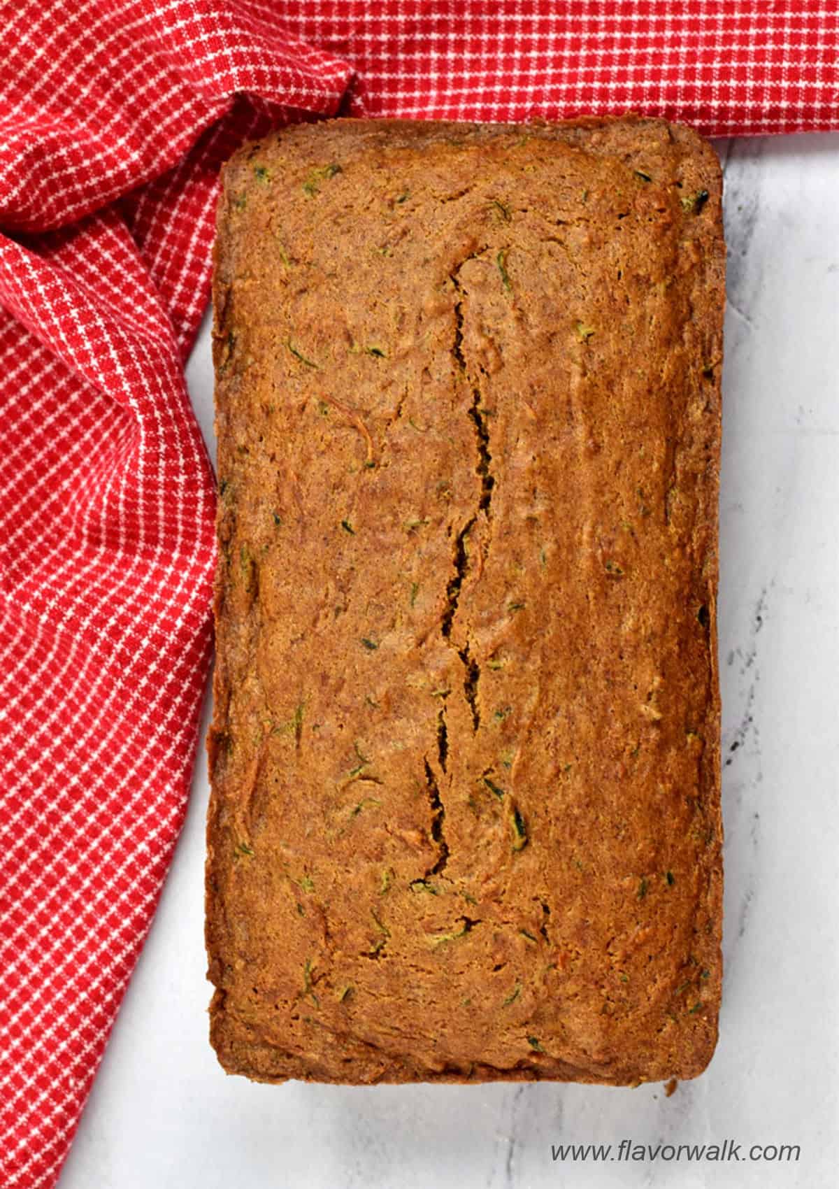 A loaf of gluten free zucchini bread and a red and white kitchen towel on the counter.