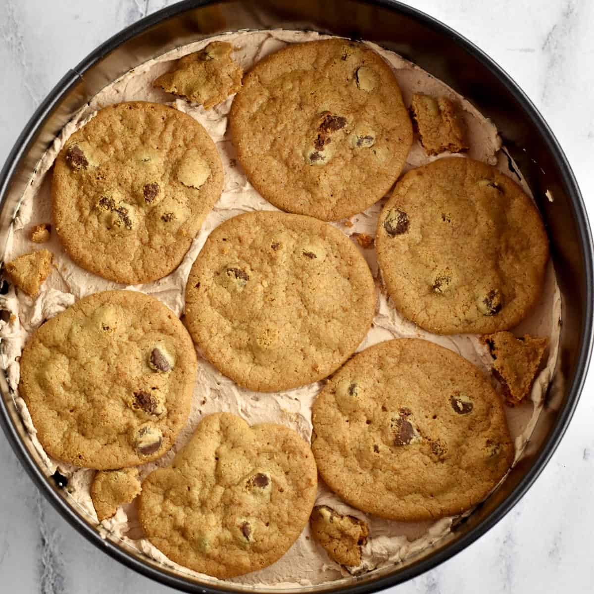 A springform pan with the first 3 layers of gluten free chocolate chip cookies and chocolate whipped cream for Old-Fashioned Chocolate Icebox Cake.