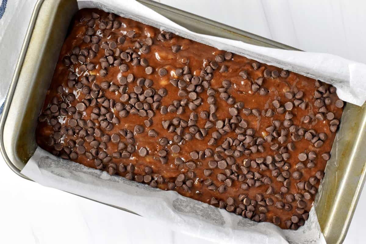 Gluten free chocolate banana bread batter in parchment-lined loaf pan.