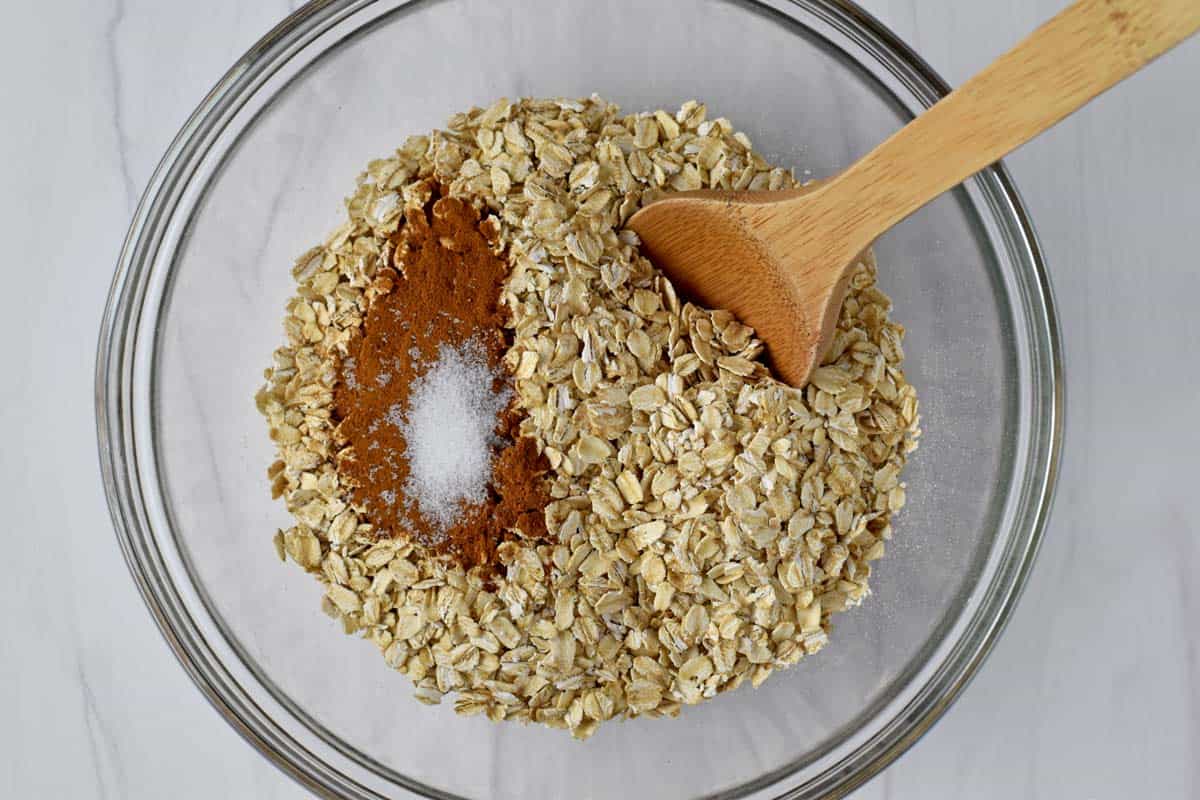 gluten free rolled oats, cinnamon, salt, and wooden spoon in a glass mixing bowl.