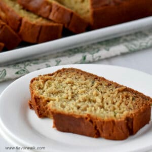 A slice of gluten free zucchini banana bread on a small white plate with the remaining loaf in the background.