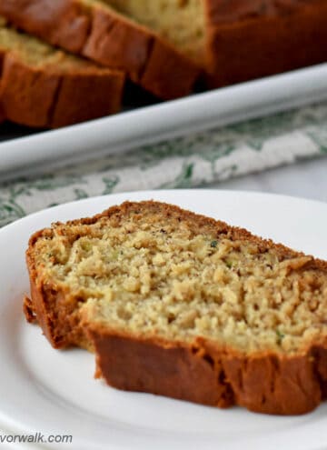 A slice of gluten free zucchini banana bread on a small white plate with the remaining loaf in the background.
