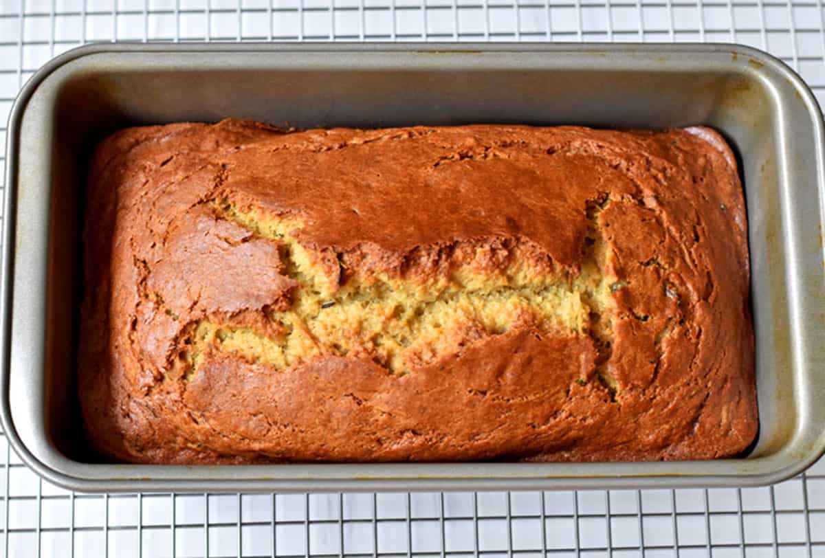 Baked zucchini banana bread in loaf pan cooling on wire rack.
