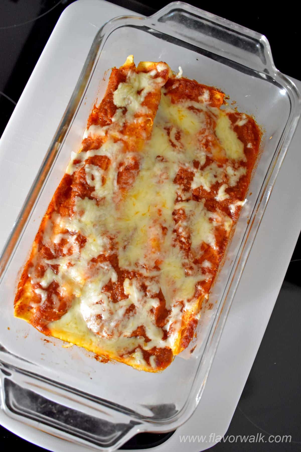 Baked chicken enchiladas for two in glass baking dish on a white cutting board.