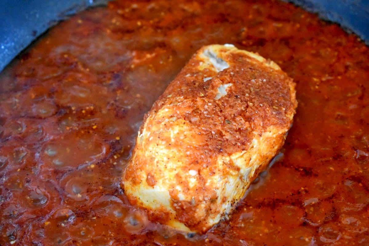 A boneless, skinless chicken breast poaching in enchilada sauce.