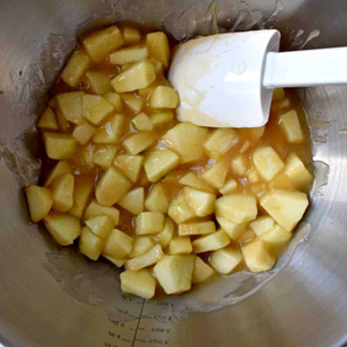 Peeled and diced Granny Smith apples, apple juice, sugar, gluten free flour, lemon juice, and vanilla mixed together with a rubber spatula in a metal mixing bowl.