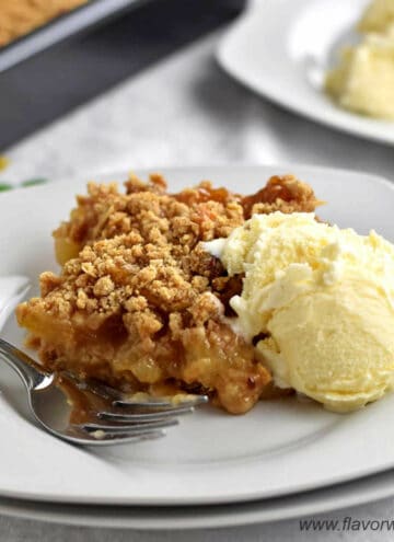 One serving of gluten free apple dessert with a scoop of ice cream and a fork on a stack of 2 white dessert plates with more apple dessert in the background.