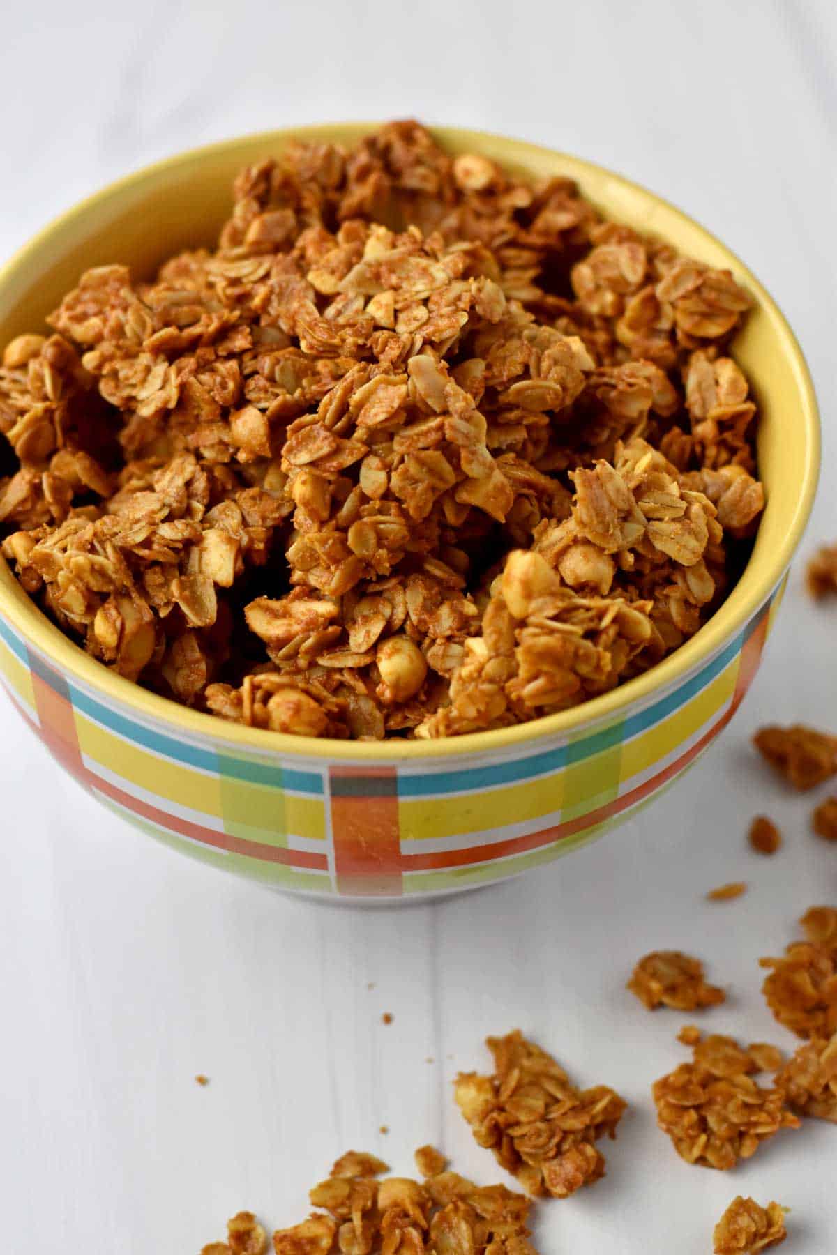 A bowl of peanut butter granola with a few granola chunks scattered on the counter.