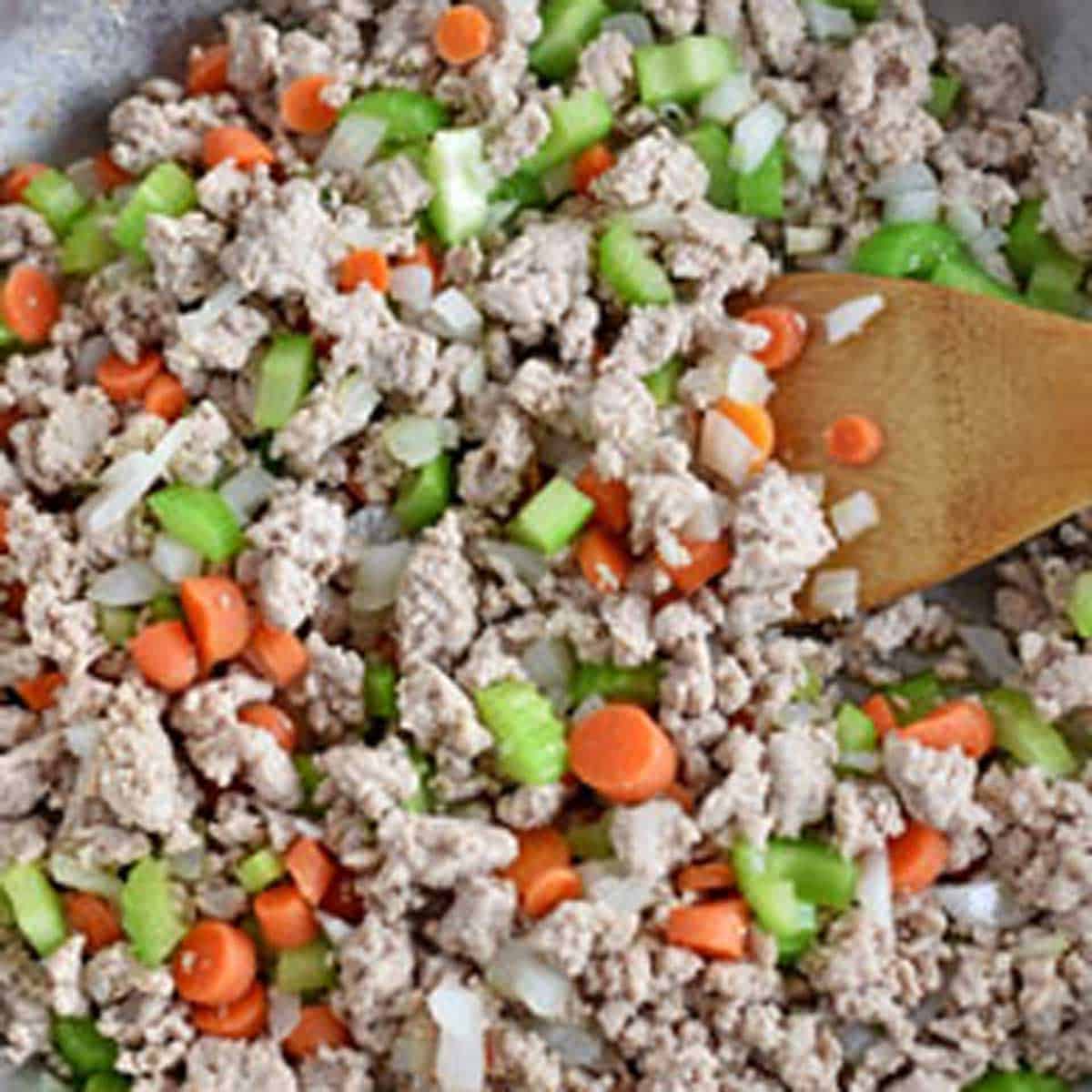 A large skillet filled with cooked ground turkey, diced onions, celery, and carrots.