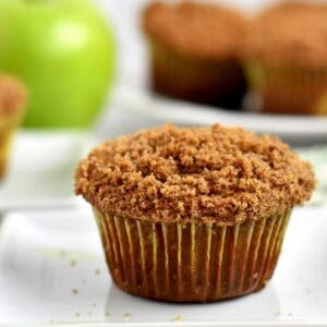 A gluten free apple muffin on a white dessert plate with more muffins in the background.