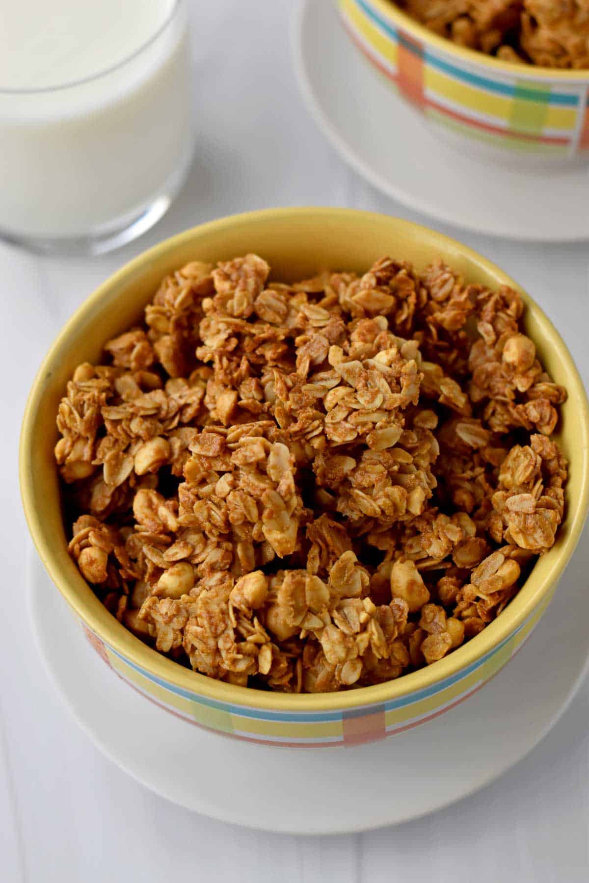 Two bowls of peanut butter granola and a glass of milk on counter.