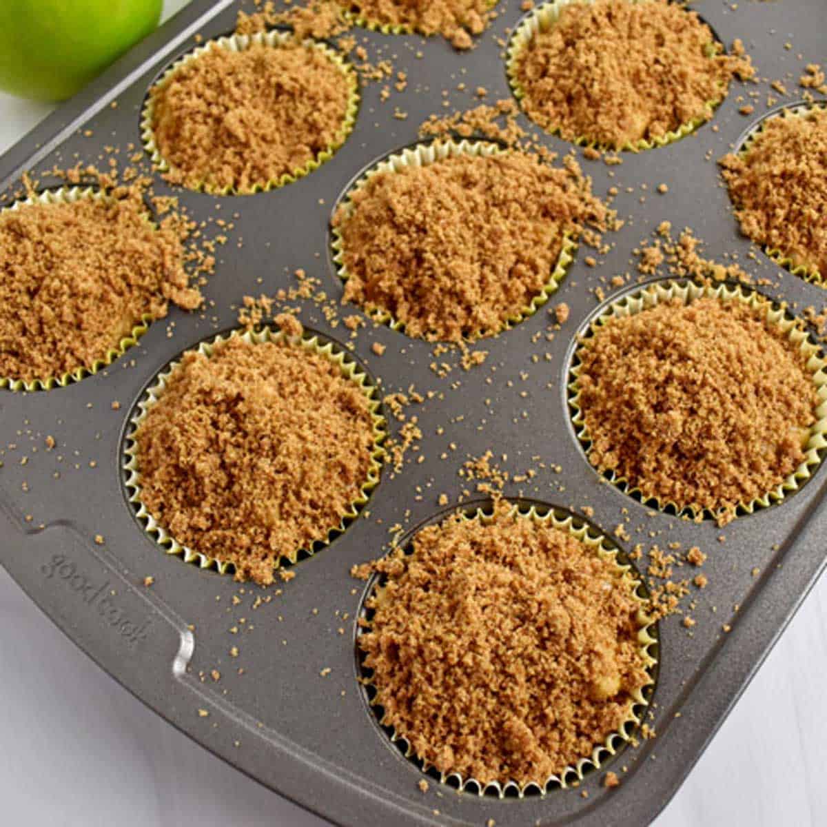 Unbaked gluten free apple muffins with crumb topping in a lined muffin pan.