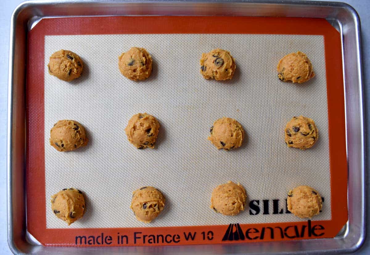 Dough balls of gluten free chocolate chip pumpkin cookies on lined baking sheet.