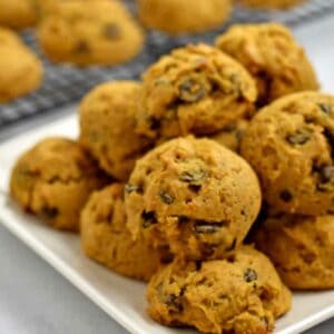 A plate of gluten free chocolate chip pumpkin cookies with more cookies on a wire rack in the background.